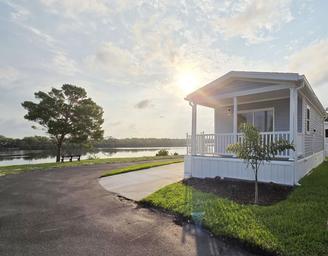 Front exterior of a cottage home with river in the background at sunset; highlights available homes/cottages and the waterfront setting (used on the resort page as a river-view home image).
