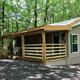 Cabin with a covered wooden porch surrounded by green forest