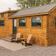 Clear photograph of a wooden tiny log cabin with porch chairs and gravel pad — shows on-site cabin accommodation; sourced from the property homepage/gallery.