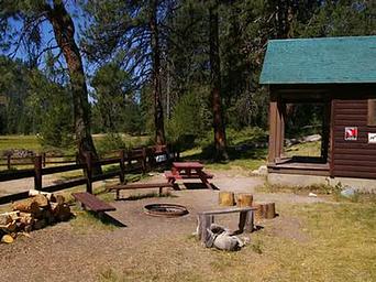 A picnic table, benches, and a fire ring next to a rustic cabin.