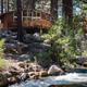 Another riverside/lodge view: close-angle of a cabin and deck above the creek with boulders and trees (from site’s 'General 2' gallery) — useful for highlighting creekfront lodging.