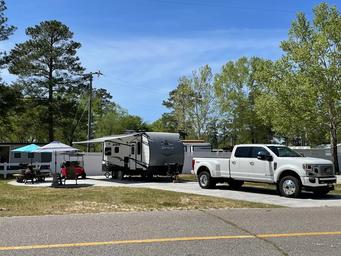 Clear daytime photo of an RV pitch with truck, awning and picnic setup — shows typical RV site layout and road access on the property (from the site gallery).
