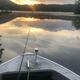 View from a boat with fishing rod toward a calm, reflective lake at sunrise/sunset — used in the site’s Activities/gallery to illustrate on-water recreation at Forest Lake.