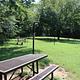 A picnic table sits on a green lawn with other picnic tables and trees in the background.
