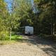 A travel trailer parked in a gravel campsite, surrounded by trees.