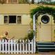 Exterior photograph of a yellow vintage trailer with a white picket fence and planted greenery — clear view of an individual lodging unit and site character from the property gallery page.