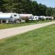 Row of RVs/trailers along a gravel road with grassy sites and utility hookups visible — shows the campground’s RV/trailer pitch area from the gallery.