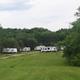 Wide view across a grassy field to a row of RVs and campsites — good overview of site layout and surroundings (Accommodations / group events page). 