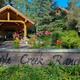 The entrance to Triple Creek Ranch features a wooden sign framed by flowers, with a covered log pavilion and pine trees in the background.