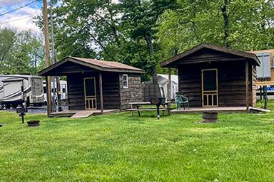 Photo of two small wooden cabins on grassy sites with picnic table and nearby RVs — directly shows the property’s cabin lodging option (page context: cabins).