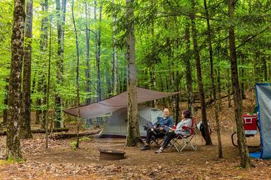 Tent campsite in a wooded setting with gear and a firepit — useful campsite lifestyle image from the campground's 'ways to stay' photos.