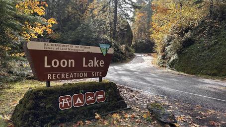 View of Loon Lake Recreation Site entrance sign in the foreground with the entrance road in the background
