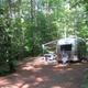 Airstream-style RV parked at a shaded campsite showing an RV pitch, awning and site layout among trees — good example of RV accommodations on site. Source: homepage gallery.