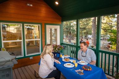 Cabin/porch dining shot showing a cabin porch with table and view of the park in background — useful to illustrate cabin accommodations and surroundings.