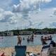 Beach/lake scene with people and RVs in the background — clearly shows the on-site swim/rec area and shoreline activity referenced by the site images.
