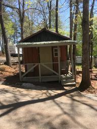 Small cabin exterior with nearby RVs and trees, showing typical cabin placement and campground roadway — useful for illustrating site layout and lodging options.