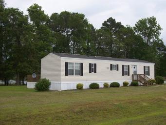 Large, well-framed photo of a rental/mobile home on grassy lot with trees and lake visible behind — useful to illustrate on-site rental housing (source: Rentals page, rentimages/3.jpg).