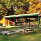 Covered picnic pavilion with multiple picnic tables and a central firepit area — shows group picnic/amenity space featured on the campground’s page.