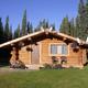 Log cabin with wooden porch and flower baskets, set in a sunny pine forest clearing