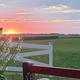 Sunset vista over open fields with white fence and part of a porch visible — illustrates scenic grounds and rural setting on the property page.