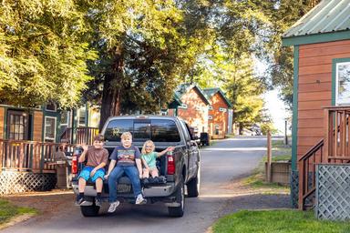 Photo showing cabins along a roadway with vehicles and people (family on truck) — another on-site view that demonstrates the look and feel of the cabin area and driveways.