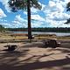 Paved campground with view of the lake and a stand up grill with picnic table and fire ring