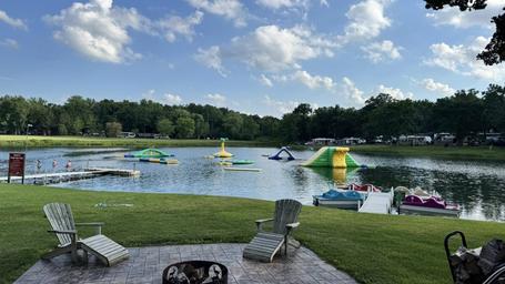 Wide-shot of the spring-fed lake with inflatable water park features and dock, with surrounding campsites visible — strong overview of the signature lake attraction.