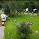 Ground-level aerial/overview of central grassy area with benches and a fire ring, showing campground communal space and nearby RVs (Photos_700x462_g2).