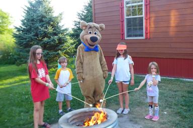 Boo Boo Bear roasting marshmallows with kids around a campfire at Jellystone Park South Haven Michigan
