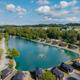 High-angle aerial view showing the campground’s central fishing pond/lake with fountain, row of cabins along the shoreline, pool and surrounding roads — matches the site’s overview imagery on the ‘Camping In Lancaster County, PA’ page.