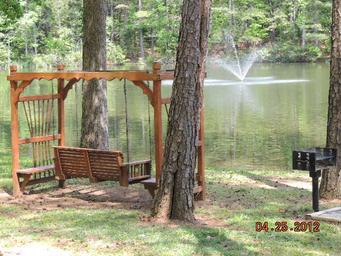 Benched swing by the lake with fountain visible — shows recreational/relaxation spot on the campground (Photo Gallery).