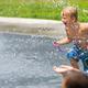 Children playing on a splash pad fountain with grassy area beyond — shows the splash-pad amenity and family activity area (homepage splash pad imagery).