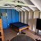 Interior of a small cabin with blue walls, bunk beds, a double bed, and a mini-fridge.