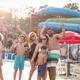Family group posing at the pool with water slides visible behind them — shows scale of pool area and guest experience at the resort’s aquatic facilities.