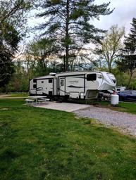 RV parked on a defined gravel/grass site with picnic table and hookups visible — clear example of RV accommodations on the property (photo from site showing actual pitch).