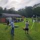 Open-field view showing the pavilion, games (cornhole), and surrounding campsites — demonstrates the campground's recreation lawn and communal spaces.