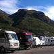 Ground-level photo of several RVs lined up on gravel pads with prominent mountain backdrop — useful for showing the RV parking/pull-through spaces and scenic context on the homepage.