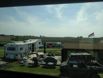 View from a building/window overlooking RVs, decks, outdoor furniture and surrounding open fields — another on-property photo hosted on the site (different vantage point from the main lawn image), useful to show site layout and surroundings.