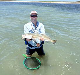 Photo of a person fishing in shallow water holding a fish — supports the park's advertised fishing/water activities and illustrates recreational use of the waterfront.