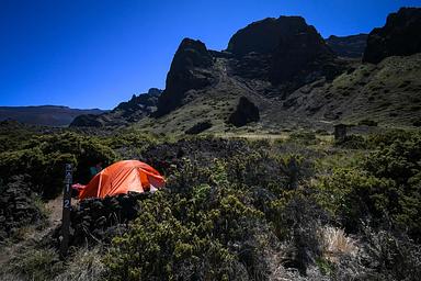 tall cliffs overlook tent site with orange tent and one camper