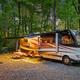 Staged RV at a gravel site with picnic table and hookups visible — directly illustrates the RV & Tent Sites shown in the site’s RV section.