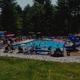 Wide, high-resolution photo of the campground’s main swimming pool with deck chairs, slide and surrounding trees — suitable as a featured amenities image; sourced from the site homepage slider.