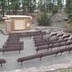 Amphitheater with brown benches and a tan building surrounded by pine trees
