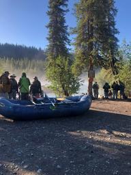 Launch/riverfront area with rafts and anglers gathering on a gravel bar — represents the campground’s river access and rafting/guide operations described on the property pages.