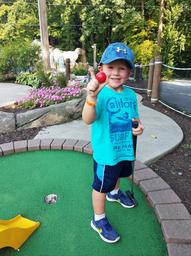 Child holding a mini‑golf ball on a putting green with landscaped surroundings — shows on‑site mini‑golf amenity and landscaped walkways. Present in the site’s activities images.