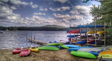 Beach scene with stacked kayaks, dock and shoreline — shows on-site water recreation and equipment storage, supporting campground amenities shown on the Map page.