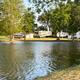 Pond with RV sites visible across the water: shows wetland edge, water reflections and RVs in the background — useful to illustrate campsite views and lakeside pitches (Activities/gallery).