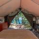 Interior of a glamping tent with bed, dresser, table, and view of water. Beige tent fabric.