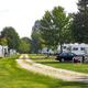Panoramic view of an RV row with parked trailers, gravel drive and grassy sites — useful for illustrating full-hookup/RV camping areas. Image is from the site (RV Row-033.jpg) and appears on the campground's pages.