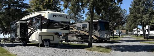 Close view of large RVs on gravel pads beneath trees — demonstrates typical full-hookup big-rig sites advertised on the property pages (slide of sites).